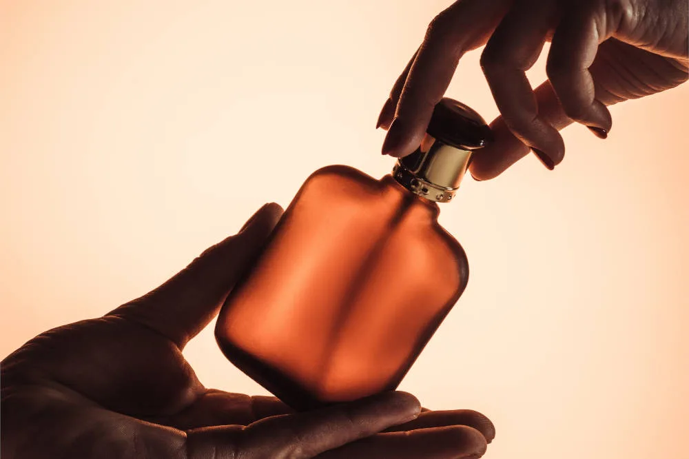 Hænder, der holder en ravfarvet parfumeflaske